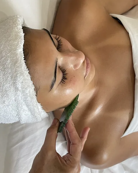 A green Gua Sha stone held along a client's jaw